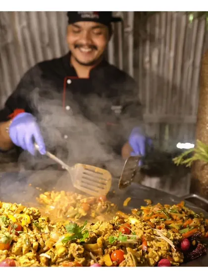 A happy chef enjoys their craft, preparing a large batch of Anda Bhurji on a tawa at a live station.