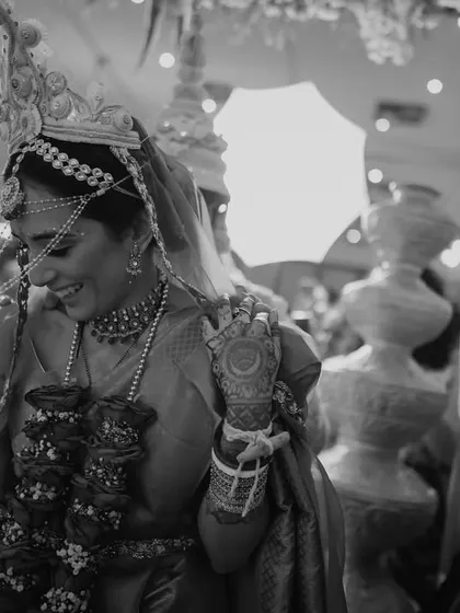 A beautiful black and white candid of a Bengali bride, her face lit up with a joyful smile as she walks through her ceremony.