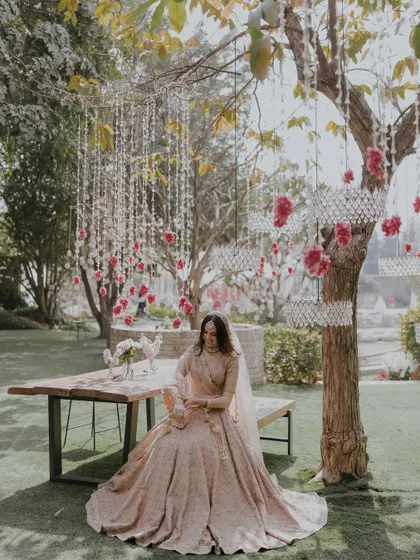 A serene portrait of a bride seated under a tree decorated with hanging crystals and flowers, a truly picturesque moment.