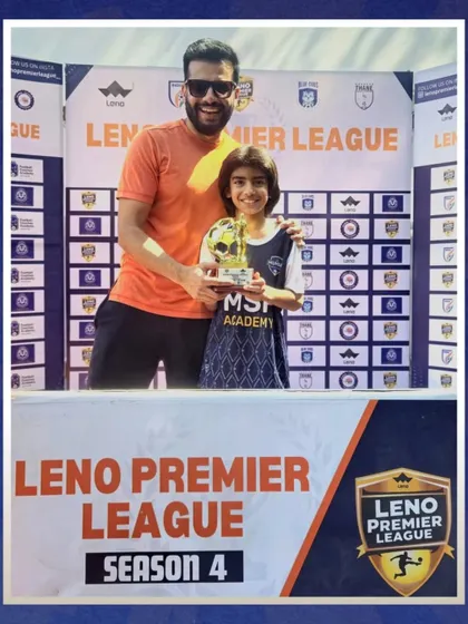 A player and coach celebrate with the Best Midfielder trophy from the Leno Premier League.