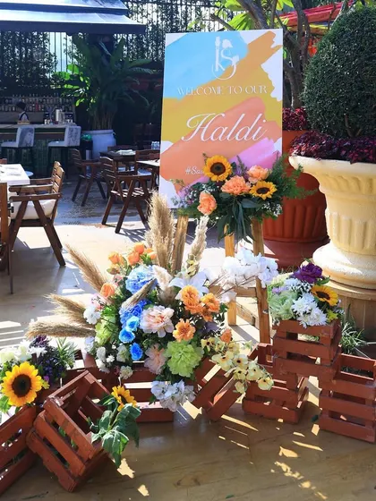 A rustic and colorful welcome setup for the Haldi. A hand-painted sign is paired with floral arrangements in wooden crates, creating a charming and inviting entrance.