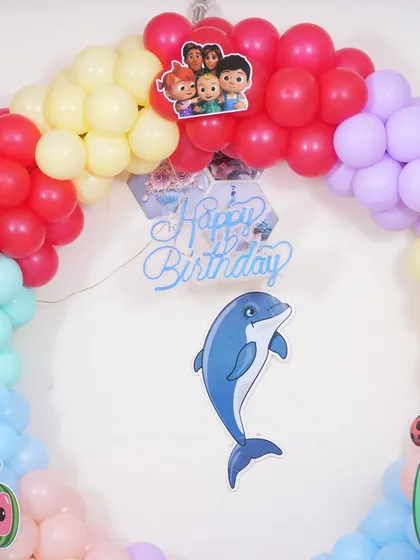 A detail shot of the top of the Cocomelon balloon arch, with the "Happy Birthday" sign and a dolphin character.