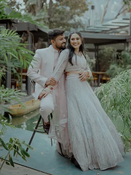 A happy couple poses by a small pond in a garden venue, their coordinated outfits shining. This shot captures the joy and style of a pre-wedding event or reception.