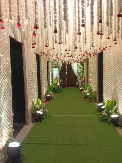 A full view of the enchanting traditional entrance corridor. The path is lit by spotlights, highlighting the intricate latticework walls and the dense canopy of hanging flowers above.