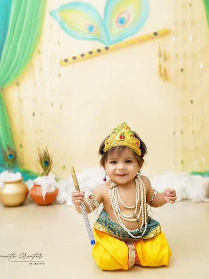One of our twin Krishnas, ready for some playful mischief. The vibrant backdrop with peacock feathers and flute illustration adds to the festive feel of the shoot.