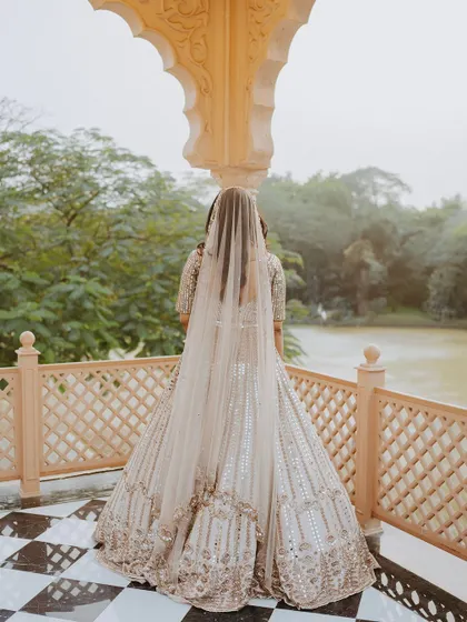 A bride stands on a balcony overlooking a lake, her long veil trailing behind her, creating a sense of quiet contemplation.