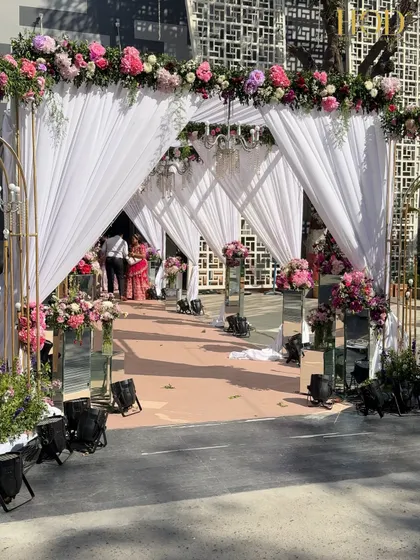 A full view of the white draped entrance tunnel. The soft fabric, floral headers, and hanging chandeliers create a dreamy and ethereal pathway, perfect for a romantic wedding reception.
