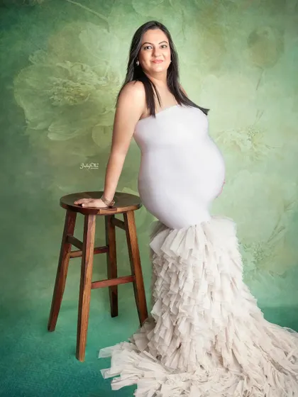 A simple and elegant pose against a lovely green floral backdrop. This mama-to-be looks so graceful leaning against the stool in her beautiful white mermaid gown.