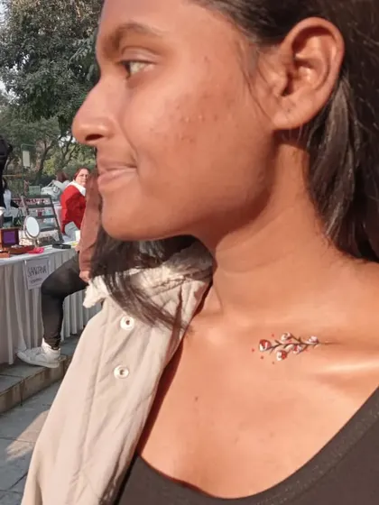 A small, delicate branch with red berries painted on the collarbone. It's a subtle yet beautiful piece of body art.