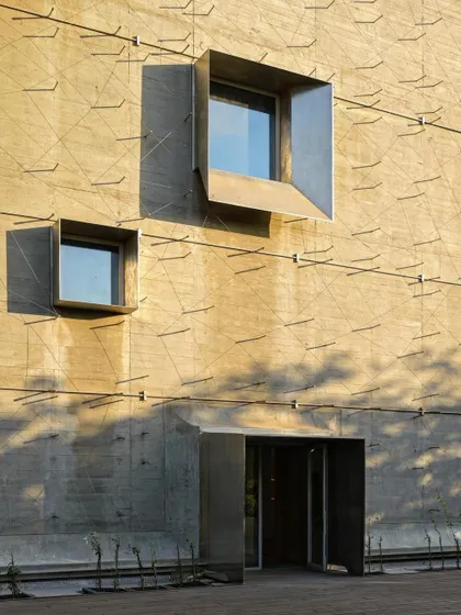 Operable steel window boxes are set within a raw concrete facade. These apertures act as both windows and shading devices, and their sculptural quality adds a fine-grained detail to the monolithic wall.