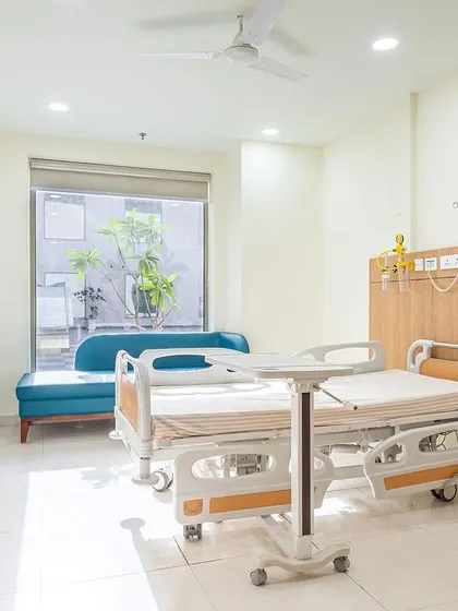 This patient room at Sarvesh Health City features a large window with a view of the outdoors. The design prioritizes natural light and a connection to nature, which are essential for creating a healing environment.