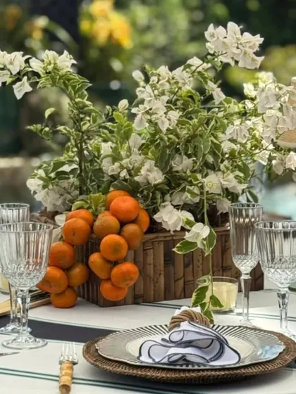 A fresh and vibrant tablescape detail from a garden lunch. The centerpiece combines white bougainvillea with clusters of oranges in a rustic wooden box, perfectly capturing a Mediterranean feel.