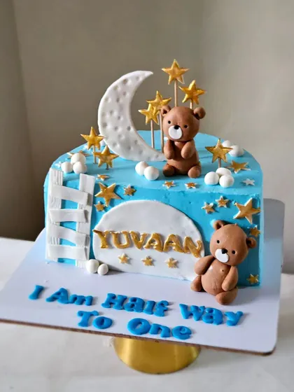 A sweet cake to celebrate being "Half Way to One." This design features a moon and stars theme, with two cute teddy bears and a ladder climbing up the side of the cake.