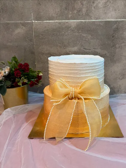 A full view of the two-tier minimalist cake with a gold ombre effect, showing how the large, delicate bow serves as the central focus of the design.