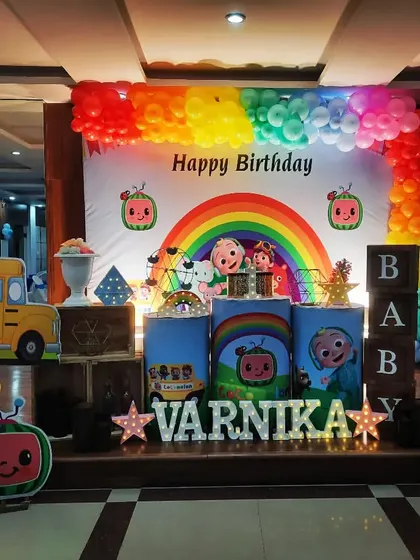 Another fantastic Cocomelon setup, this time for Varnika. The decor features a full rainbow balloon arch and multiple character cutouts, creating a vibrant and joyful scene.
