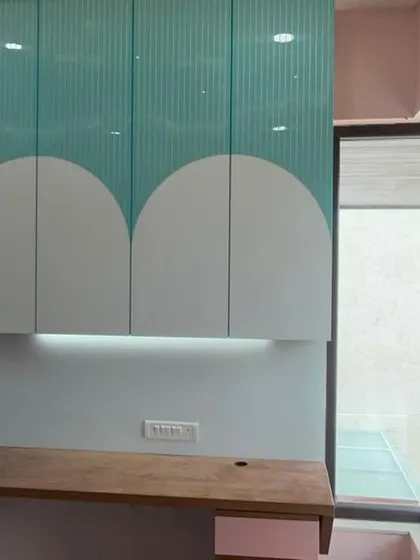 A custom-designed study and storage unit for a kids' room. The playful, scalloped cabinet design in teal and white adds a fun touch, while the wooden desk provides a sturdy workspace.