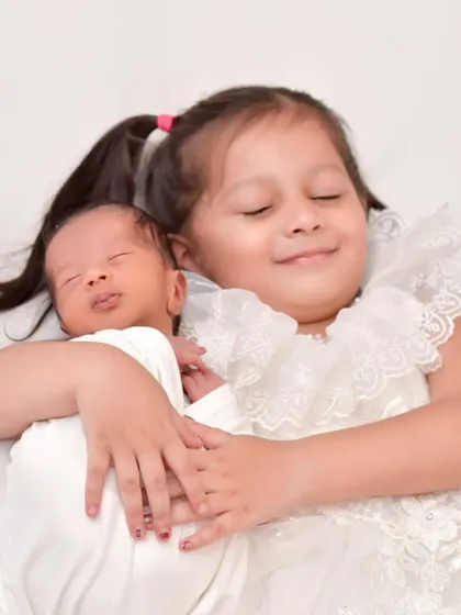 An angelic portrait of an older sister with her eyes closed in a happy smile as she lovingly hugs her newborn sibling, capturing a moment of pure sibling love.