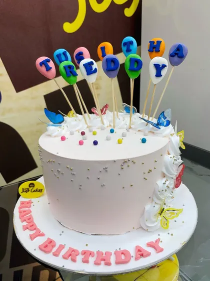 A festive 2kg birthday cake with colorful balloon toppers and butterfly accents.