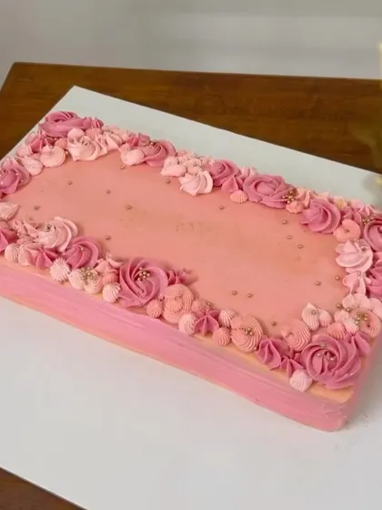 A beautiful rectangular cake in shades of pink, adorned with a cascade of delicate, hand-piped buttercream flowers. This red velvet cake was designed to be a showstopper.