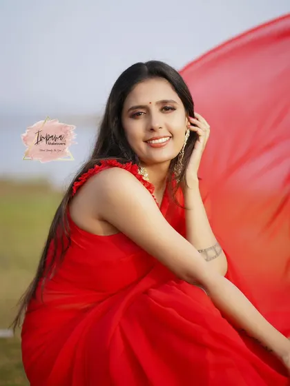 A joyful, candid shot from the red saree photoshoot. The model's natural beauty is enhanced with a glamorous makeup style.