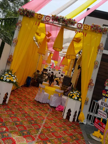 A bright and welcoming entrance for a Haldi function. The combination of yellow and pink drapes, conical hanging decorations, and floral arrangements sets a cheerful tone for the event.