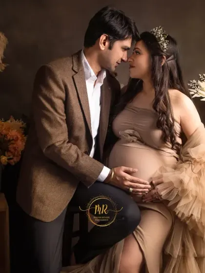 This wider shot shows the full studio setup with rustic crates and floral arrangements, which complement the earthy tones of the couple's attire for their maternity photoshoot.