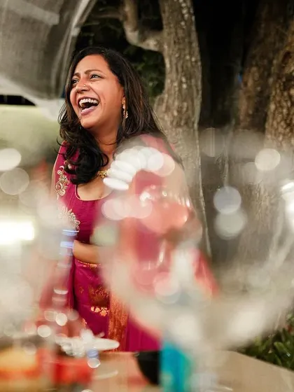 A guest's candid laughter captured through a creative foreground of glasses, adding depth to the party shot.