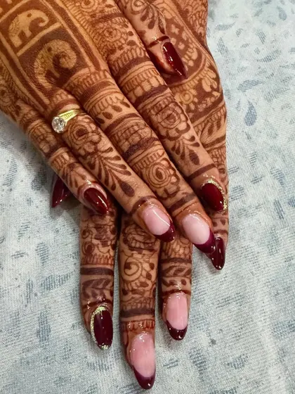 This close-up shows the detail of the deep red reverse French manicure against the beautiful bridal henna. The subtle gold glitter line adds a touch of elegance.