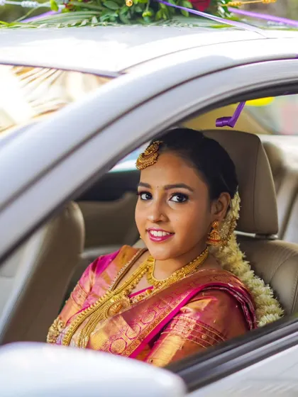 The bride, radiant in her pink silk saree, smiles from her wedding car, ready for her new journey.