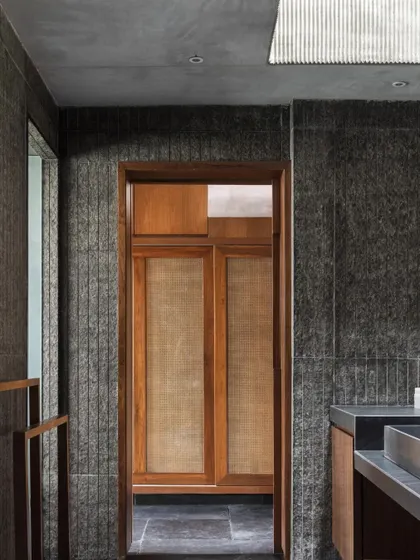 A bathroom in the Brick House, where hand-chiselled stone walls and a slatted concrete skylight create a spa-like atmosphere. The design explores the experiential qualities of raw, local materials.