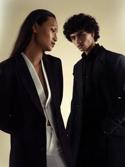 A dual-model shot for a modern, androgynous fashion campaign. The dark, tailored suits and moody lighting create a sophisticated and powerful image.