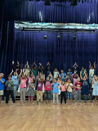 A duplicate of Image 24, this wide shot shows the entire group of summer camp children on stage, practicing a unified pose for their final performance.