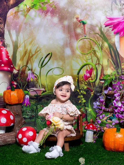 A smiling toddler enjoying our enchanted forest theme, complete with fairy houses, mushrooms, and pumpkins. Her delightful expression brings this magical scene to life.