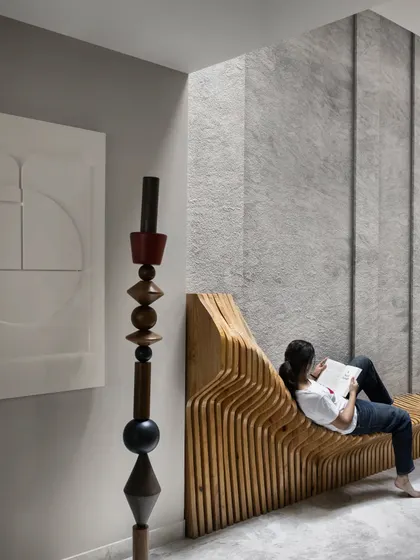 A custom-made wooden sculptural bench in the Slender House dining area serves as both an art piece and a utilitarian feature. The fluid lines of the seating are carried forward to the ceiling and walls, creating a cohesive design language.