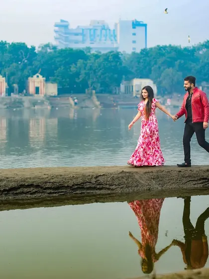 A couple walks hand-in-hand by a lake, their reflection captured in the water, creating a beautiful and romantic image.