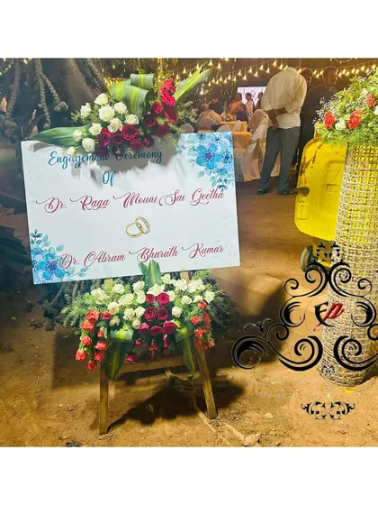 A welcome sign for a destination engagement, set up outdoors and adorned with beautiful red and white flower arrangements.