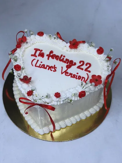 "I'm feeling 22 (Liane's Version)". A perfect cake for a Swiftie's birthday. This white heart-shaped cake is decorated with red ribbons and flowers, inspired by Taylor Swift's "Red" era.