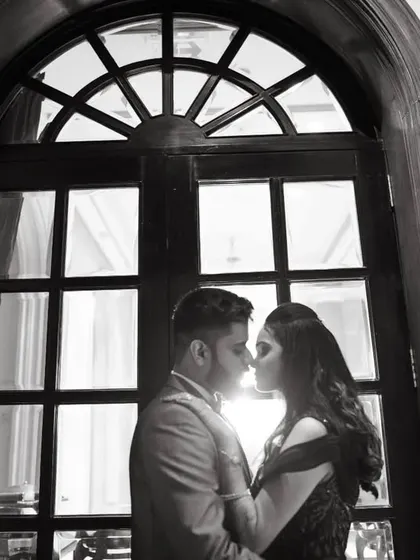 A silhouette of the couple against a large arched window, a dramatic and timeless black and white portrait.