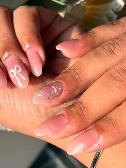 A close-up of the sheer pink manicure, showing the detail of the hand-painted white bow and snowflake designs.