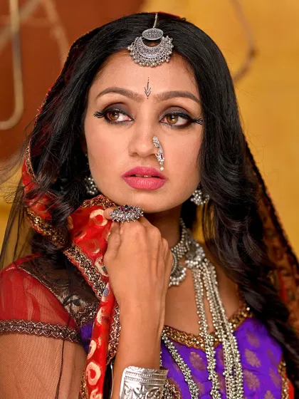 A close-up portrait focusing on the expressive eyes and the intricate details of the silver jewellery, including the maang tikka and nose ring.