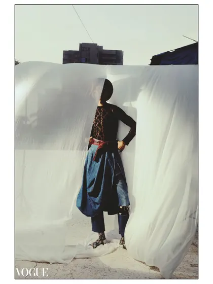 A full-length portrait shot on film for PhotoVogue, featuring a model in a gender-fluid look with a flowing denim skirt. The natural sunlight and the texture of the film create a soft, timeless image.