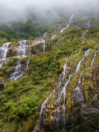 Waterfalls cascade down a mountainside, shrouded in mist, on the way to Annapurna Base Camp. This is a common sight on our Himalayan treks, where nature's power is on full display.