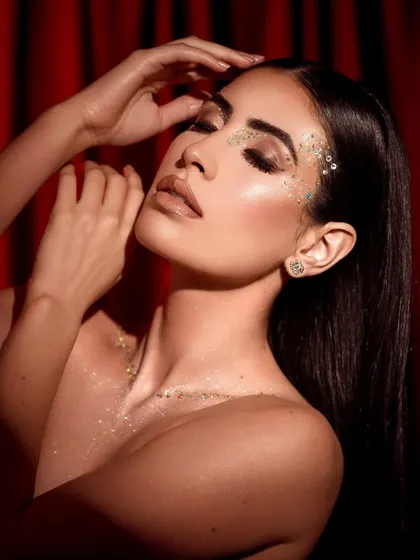 An expressive and glamorous pose, with eyes closed to showcase the glittering makeup artistry on the eyelids.
