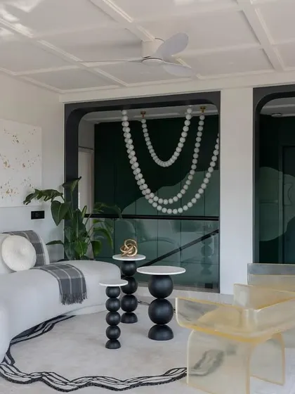 This view of the Evelyn lounge highlights the unique combination of furniture and art. The transparent resin chairs add a modern touch, while the pearl necklace chandelier provides a dramatic backdrop.