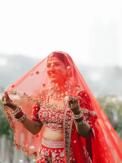 A beautiful, happy bridal portrait with her red veil flowing in the breeze. Her genuine smile captures the pure joy of her wedding day.