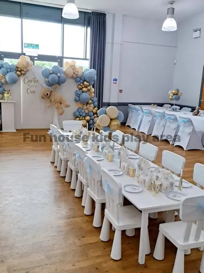 An elegant indoor setup for a first birthday party. Our white tables and chairs are beautifully arranged, complementing the sophisticated blue and gold balloon decor.
