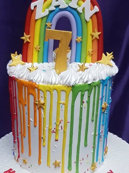 A vibrant rainbow drip cake for a 7th birthday. This cheerful design is topped with fluffy buttercream clouds and golden stars, making it a bright and happy centerpiece for any party.