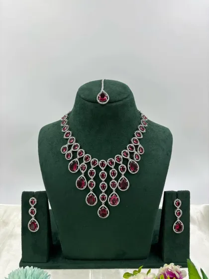 An elegant AD necklace set with a matching maang tikka. The cascading design with teardrop stones is available in green, pink, and all-white, perfect for receptions and parties.