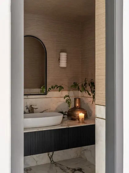 The powder room is wrapped in a combination of grasscloth wallpaper and white marble. This mix of textures creates a subtle statement, giving the small space a chic and understated vibe.