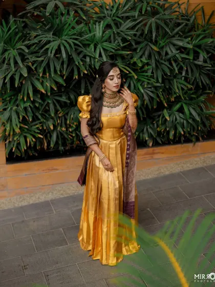 A stunning bride in a golden half-saree, perfect for a pre-wedding ceremony. The makeup is elegant with a focus on defined eyes and soft contouring.